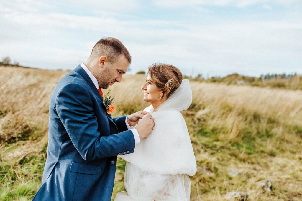 groom helping bride with shawl at autumnal wedding.